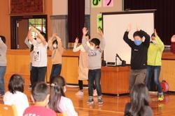 両手を上げて踊っている6年生と、座って見ている1年生の写真