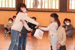 上級生が1年生の男の子に、小さな紙袋を手渡している写真