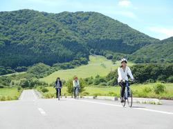 青空と雄大な山をバックにサイクリングを楽しむ人達の写真