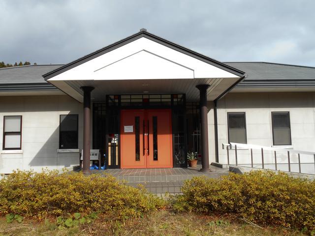 白い壁とオレンジ色の玄関ドアがある施設外観の写真