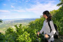 登山用のステッキを持ちながら、山間の景色を眺める登山者の写真