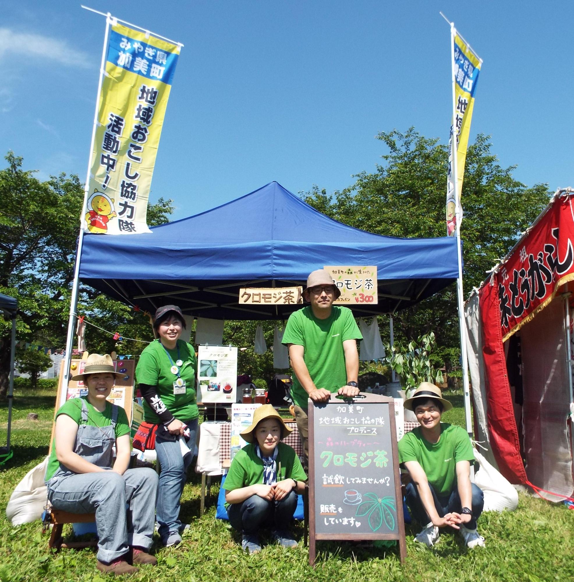 テントの前で、クロモジ茶の看板を囲んでいる加美町地域おこし協力隊の写真
