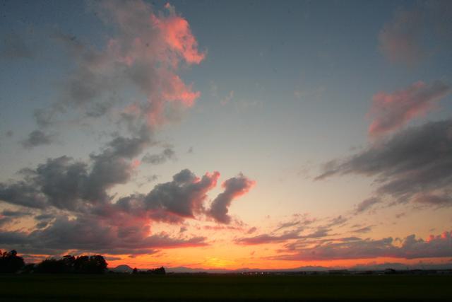 山脈の上にオレンジ色の夕日が浮かび、雲がたなびいている写真