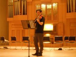 ホールで楽譜を見ながらヴァイオリンを弾いている男性の写真