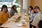 料理の皿が並んだ机を囲み、笑顔でピースをしている4人の女性の写真