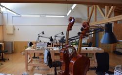手前にバイオリンが置かれており、奥に作業台がある工房の写真