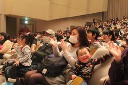 座席に座った親子連れの参加者が、拍手をしている写真
