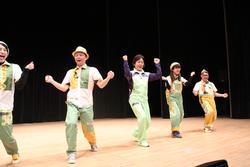 緑色の衣装を着た人たちが、舞台の上で横一列になって踊っている写真