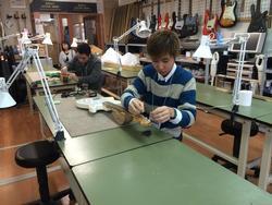 作業台に向かって、楽器に関する作業をしている男の子の写真