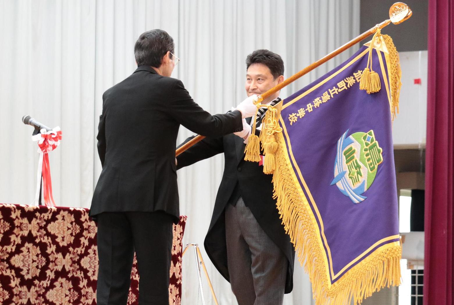 猪股町長から小野寺校長へ校旗が手渡される