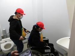 トイレの中で車いすに乗った女子児童と、後ろでサポートする男子児童の写真