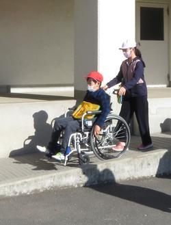 赤白帽子の児童2名がペアになってスロープで車いす体験をしている写真