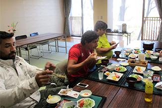屋内で座って和朝食を食べる男性三人の写真