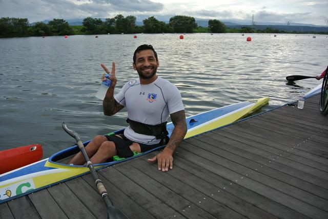 カヌーに乗って、笑顔でピースサインをしている男性選手の写真