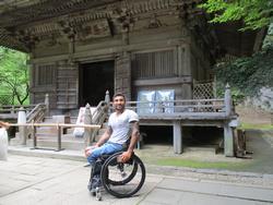 屋外でお寺の門の前で映る車椅子の男性の写真