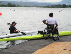桟橋の近くでカヌーを漕いでいる選手と、車いすに乗っている男性の写真