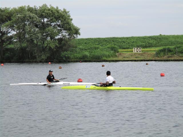黄色いカヌーに乗った選手と、白いカヌーに乗った選手が、水上ですれ違おうとしている写真