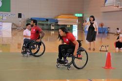 体育館で車椅子で走る車椅子の男性と女性を横から撮った写真