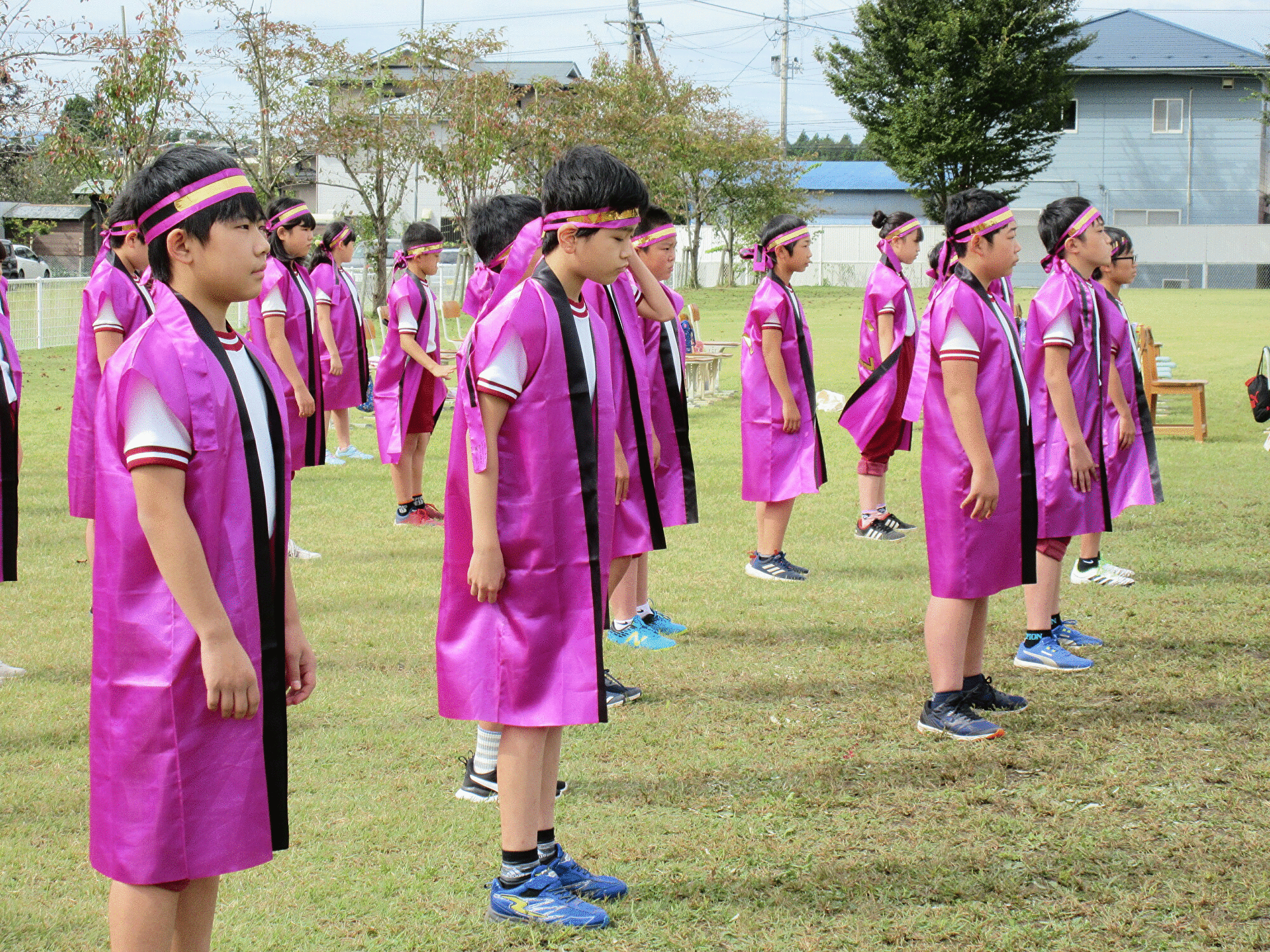 紫色のハッピを着た児童たちが校庭で並んで立っている写真