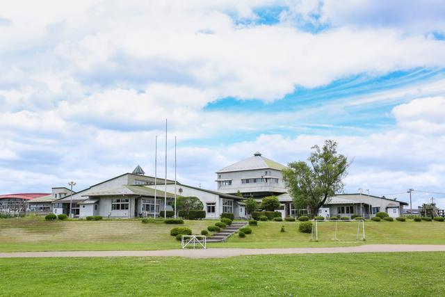緑の芝生と雲の切れ間から青空がのぞく中に建てられた鳴瀬小学校校舎の写真