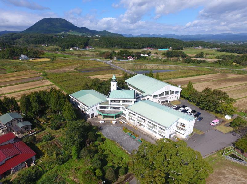 緑豊かな土地に建つ水色の屋根の校舎を上空から見下ろした写真