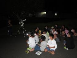 夜の屋外で子供たちが座っていて、横に望遠鏡が置かれている写真