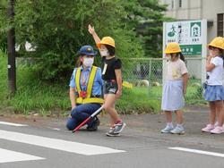 子供の目線に合わせてしゃがむ警察官の横で、片手を上げた子どもが横断歩道を渡ろうとしている写真