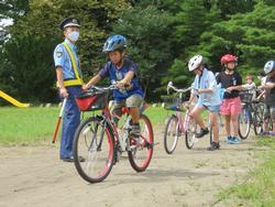 警察官の前を、子どもたちが一列に並んで自転車に乗っている写真