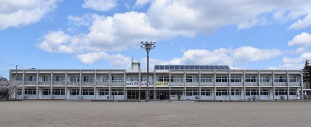 雲のある青空をバックに横に長い中新田中学校の校舎の全体が写っている写真